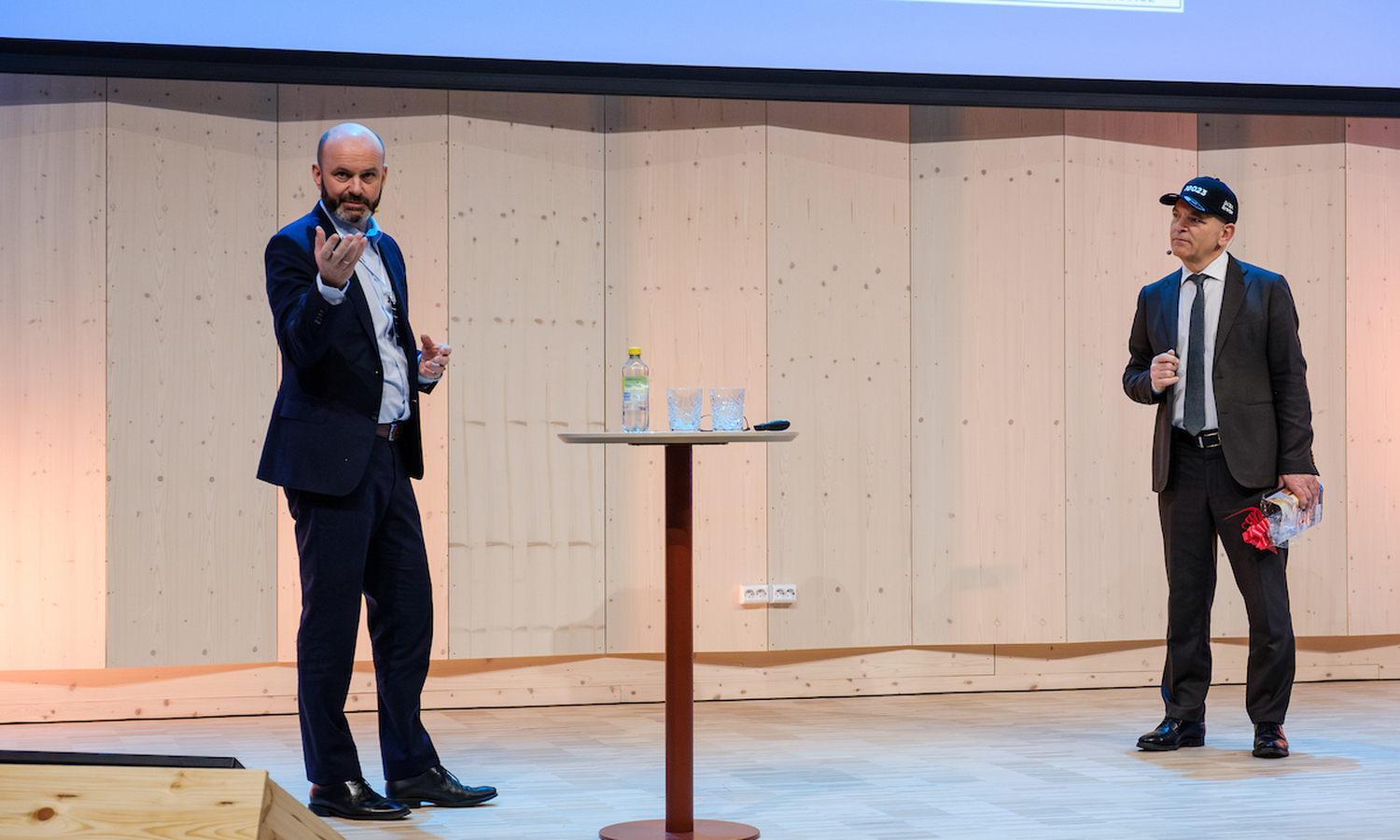 To menn i mørke dresser. Den ene med en sort caps med påskriften 10023