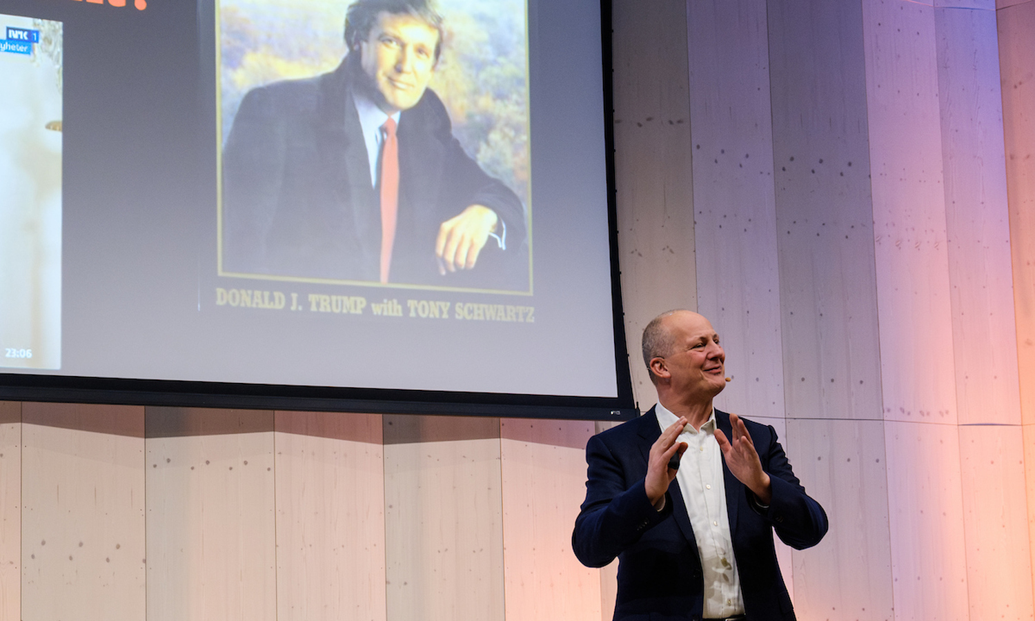 Mann i dress ser ut over publikum, og gestikulerer med armene mens han snakker