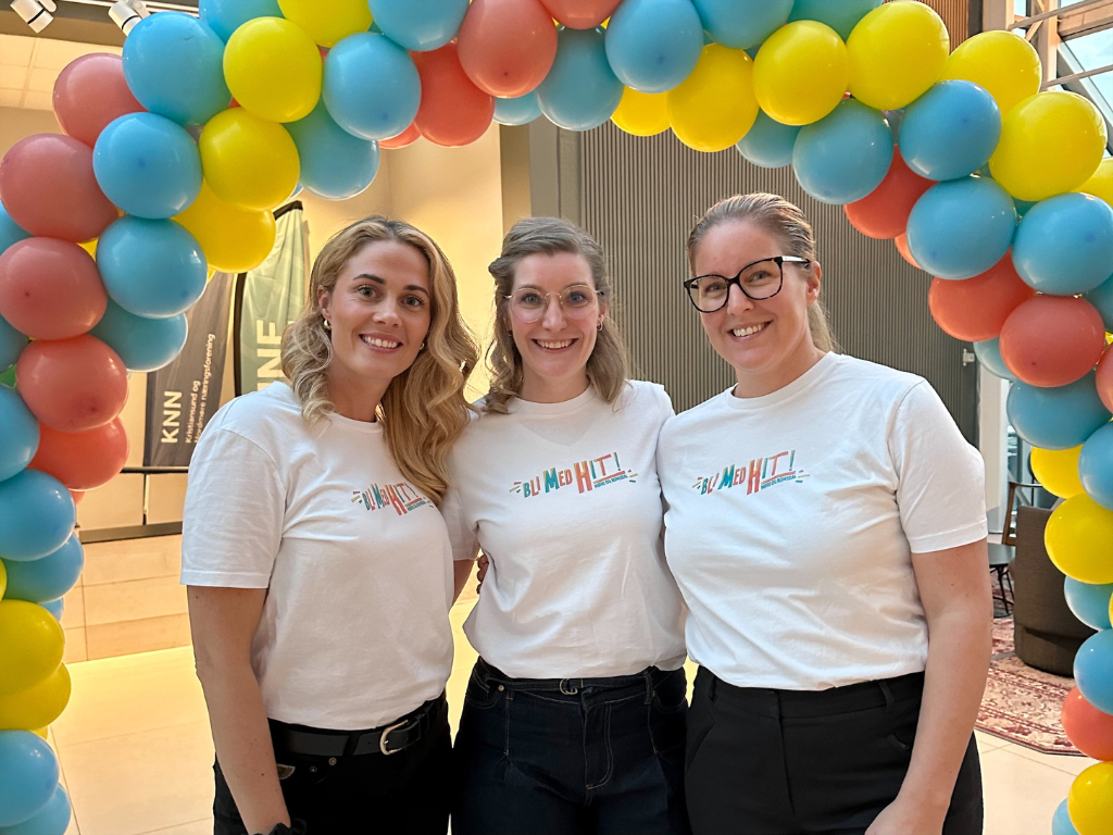 Iselin Akslen, Kjærsti Nancke og Henriette Asphol Indbjør, prosjektlederne i BLI MED HIT!  Tre kvinner i hvite t-.skjorter med påskriften BLI MED HIT, står under en ballongbue bestående av gule, røde og blå ballonger, smiler mot kamera.